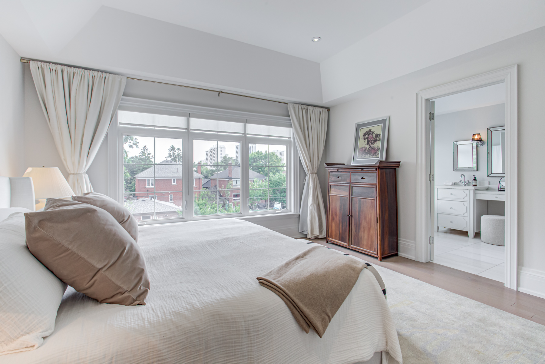 Bedroom with large windows showing view of trees and houses.