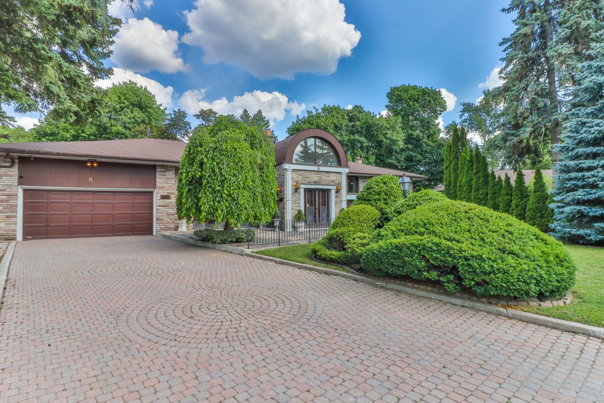 Large bungalow with 6-car driveway and huge front yard with trees.