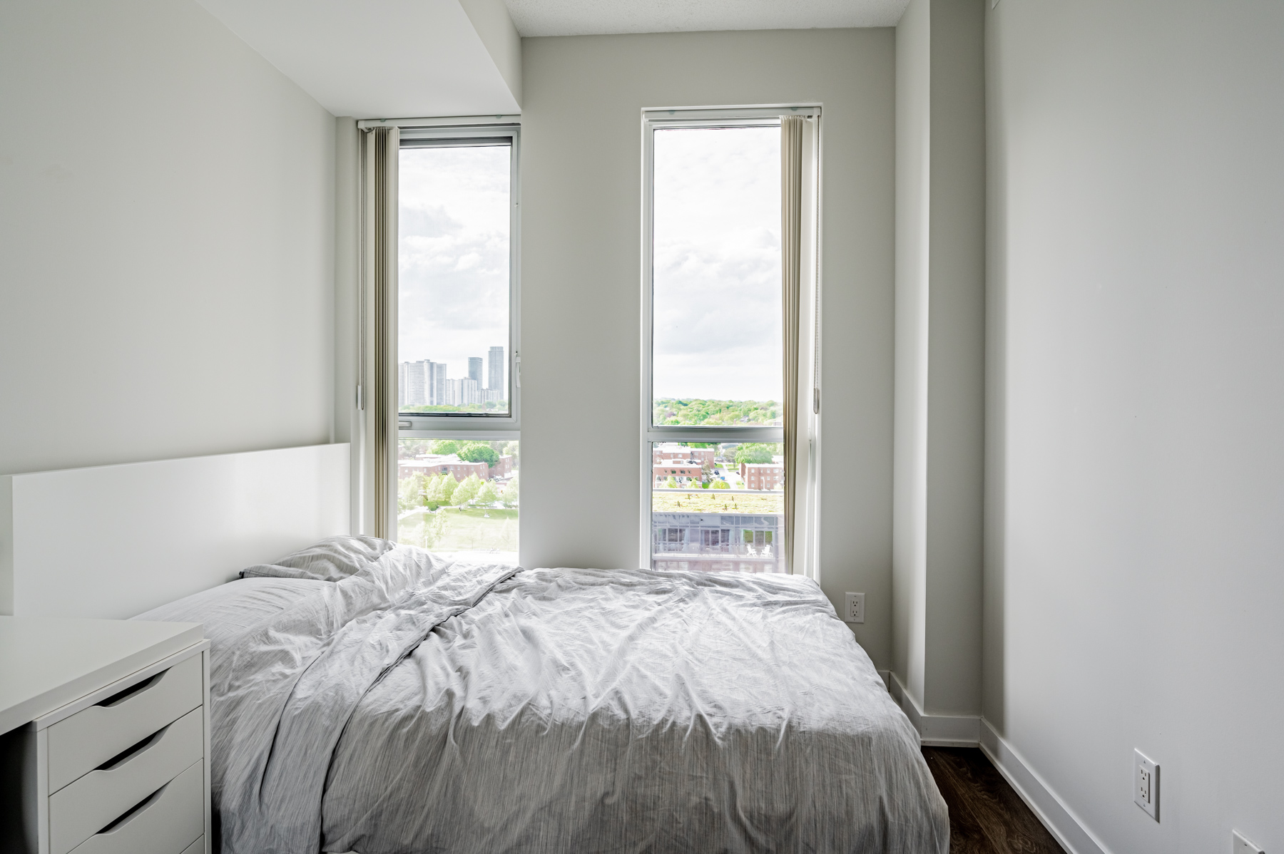 Condo bedroom with 2 tall windows with view of trees.