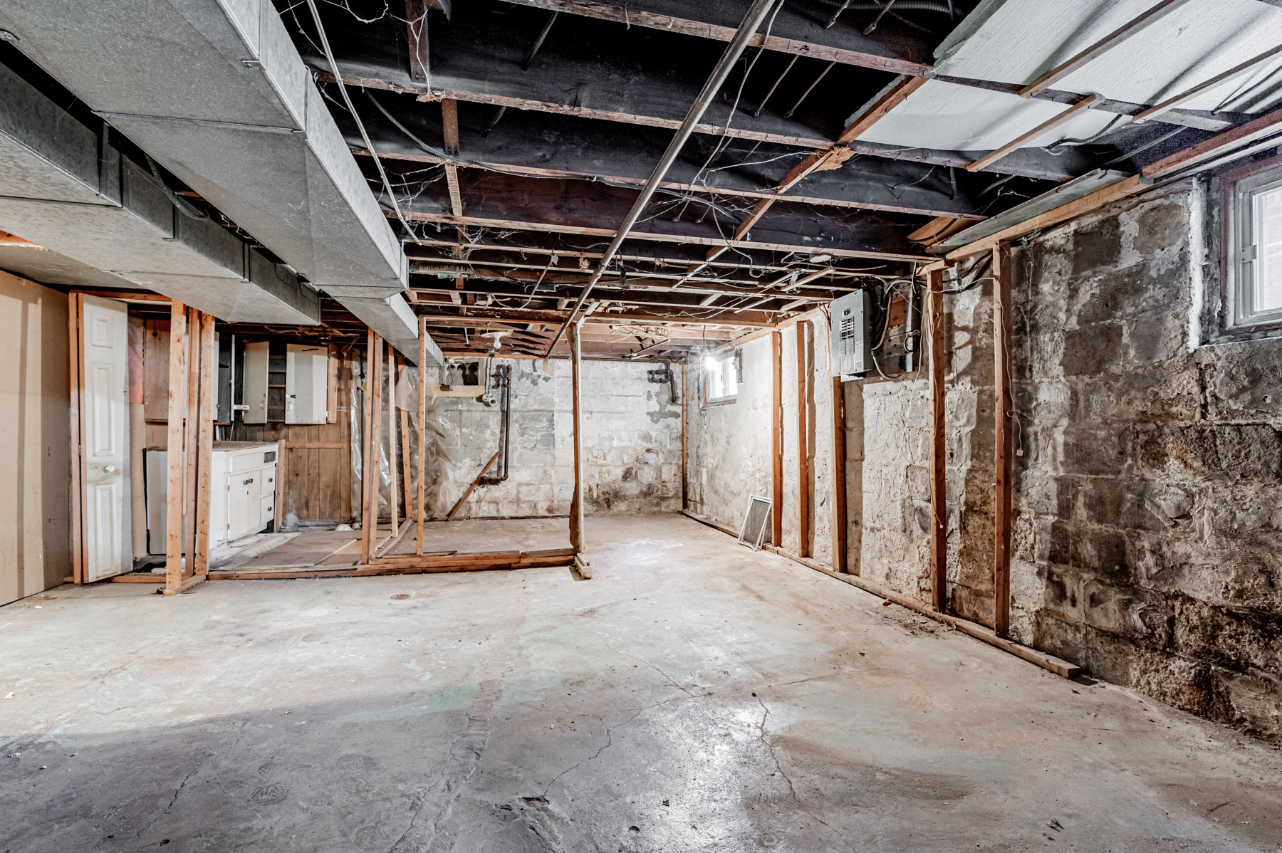 Large unfinished basement with bare walls, floors, exposed ceiling and woodwork.