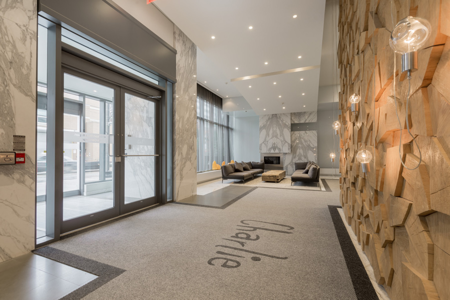 Charlie Condos lobby with high ceilings, pot lights, carpeted floors and light bulbs hanging from a rock-wall.