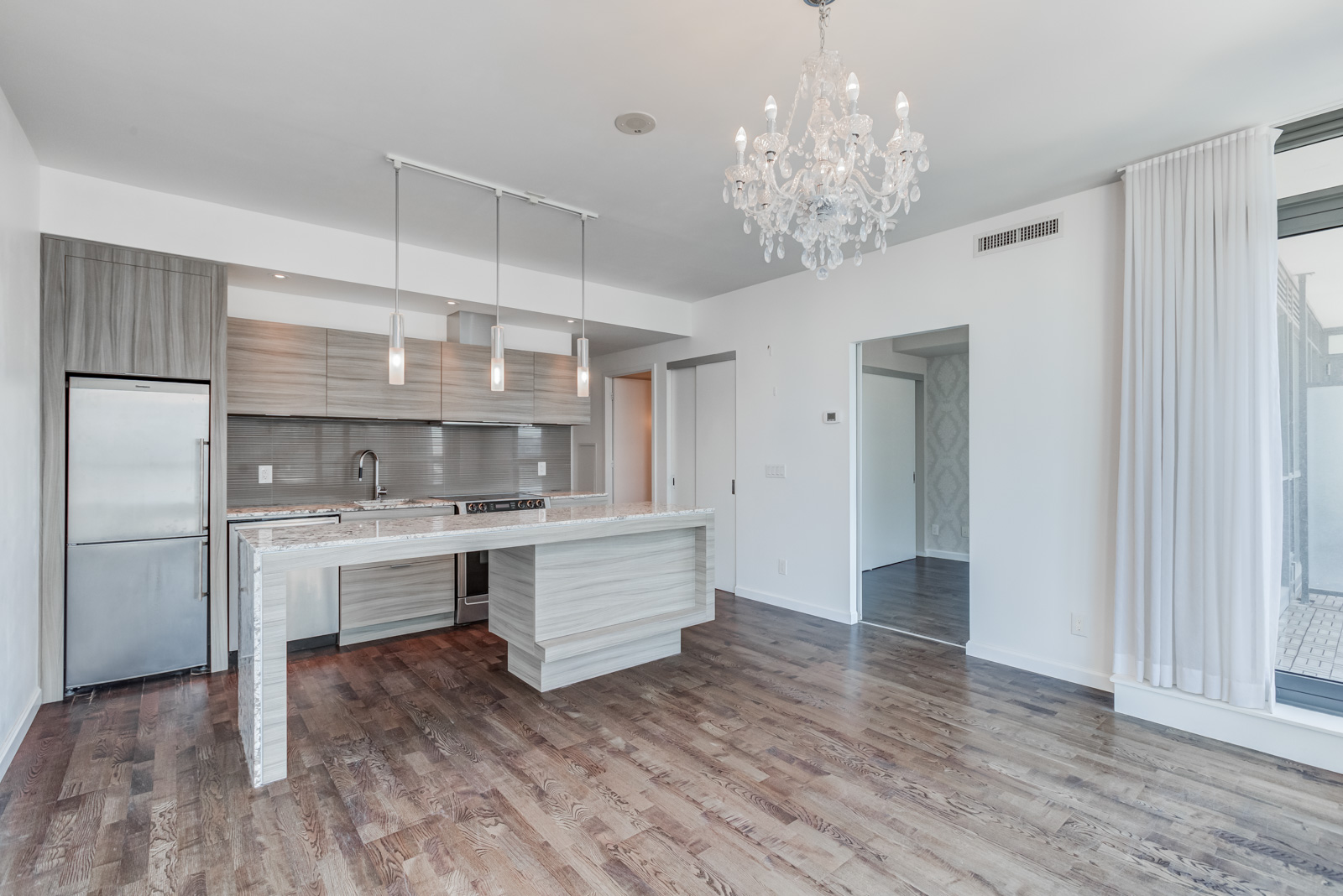 Open-concept living room, dining room and kitchen with chandelier, kitchen island, and wooden laminate floors.