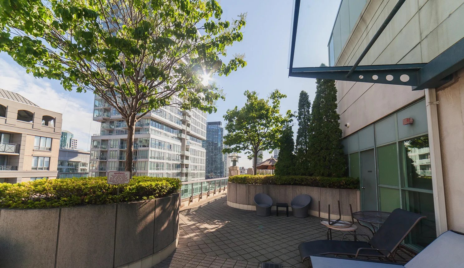 168 Simcoe St's rooftop deck with chaise lounges, shrubbery and view of downtown Toronto.