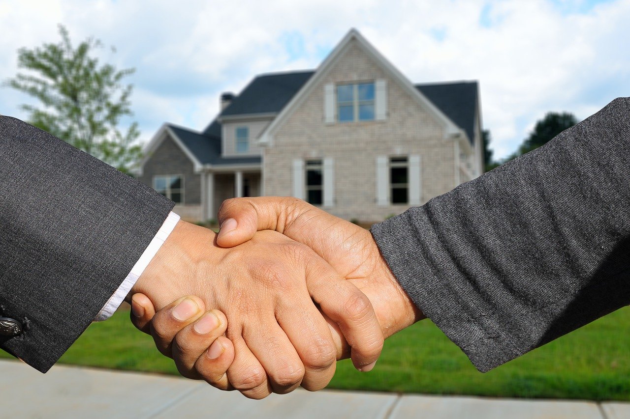 2 men in gray suits shaking hands with house in background showing strength of 2020 spring market.