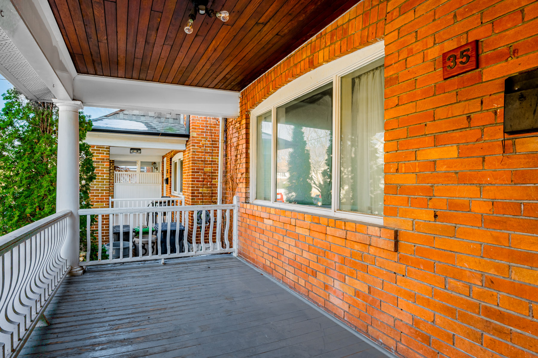 House with red-brick facade, white railing and wooden porch.