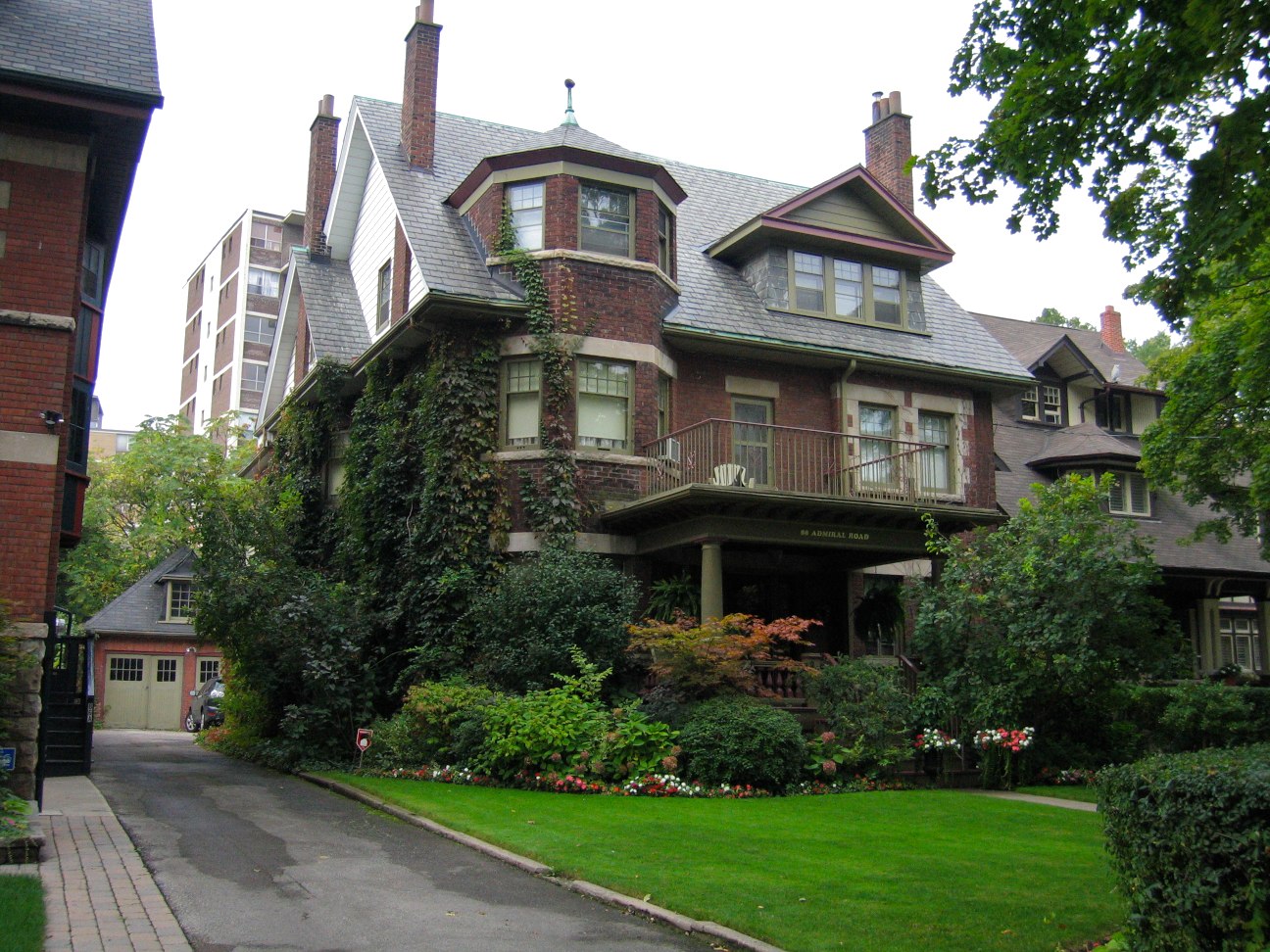 Brown Victorian mansion with green lawn, shrubs and ivy on Bathurst and Bloor West in The Annex neighbourhood.