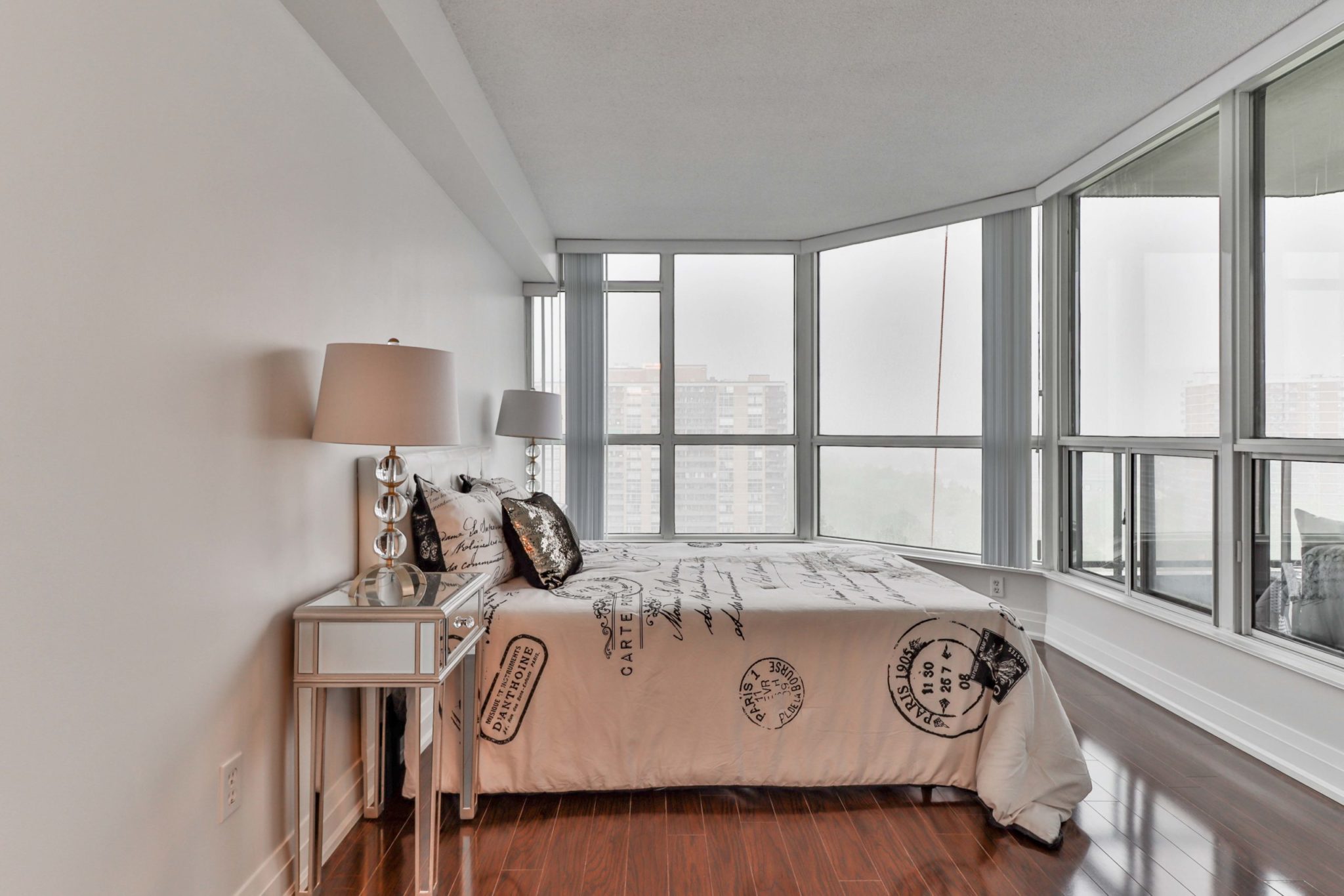 Condo bedroom with large windows and shiny laminate floors.