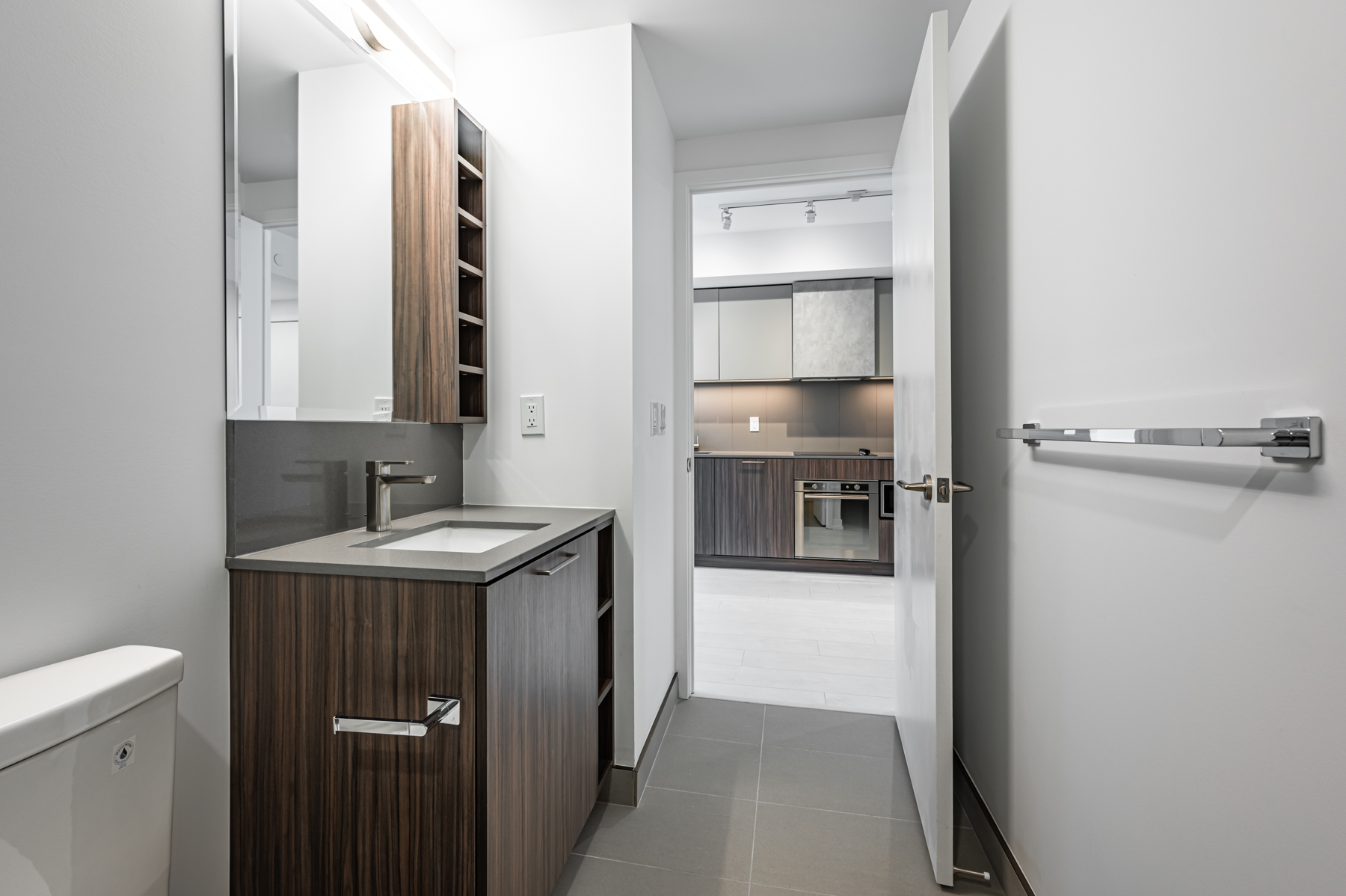 Condo bathroom with ceramic floors, gray back-splash, cubbies and big mirror.