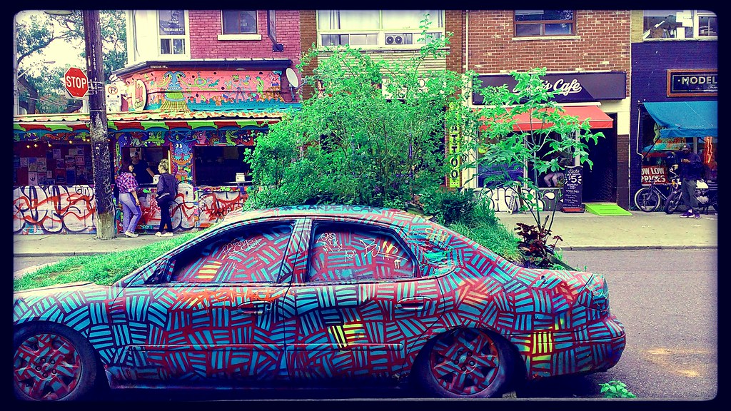 A graffiti-painted car and colourful shops in Toronto's Kensington Market.