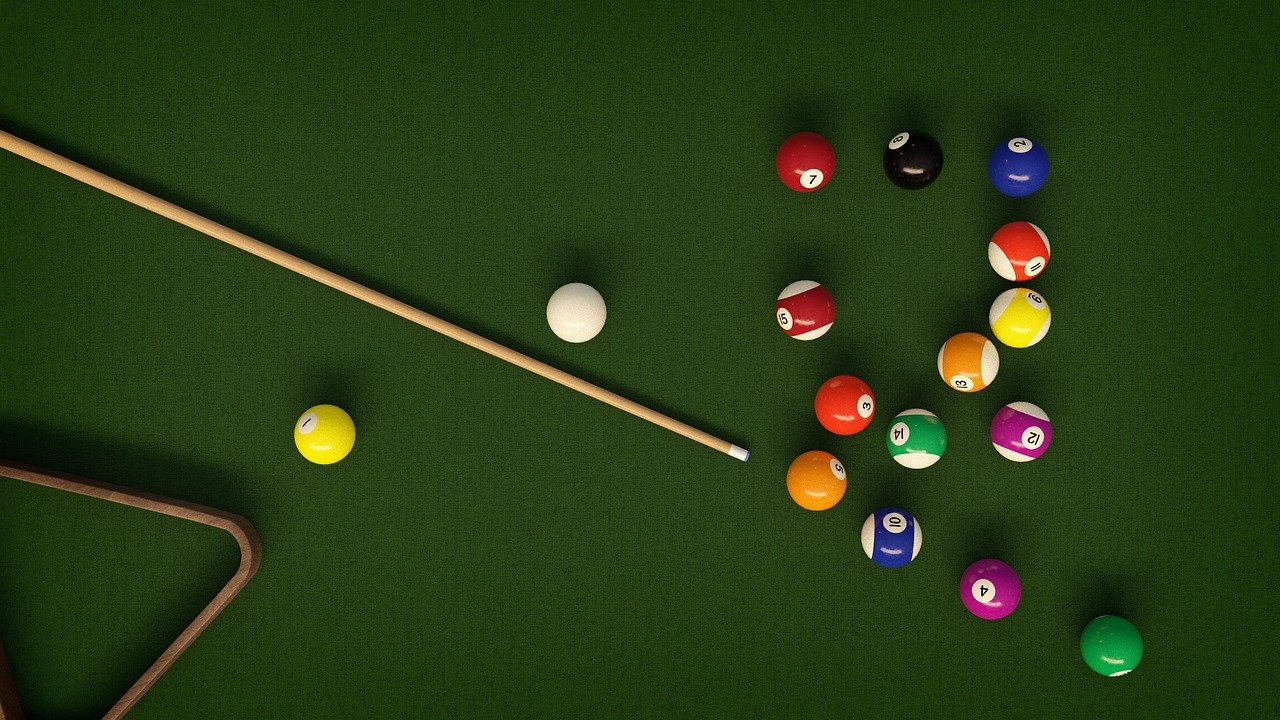 Top down view of billiards table with balls and cue.