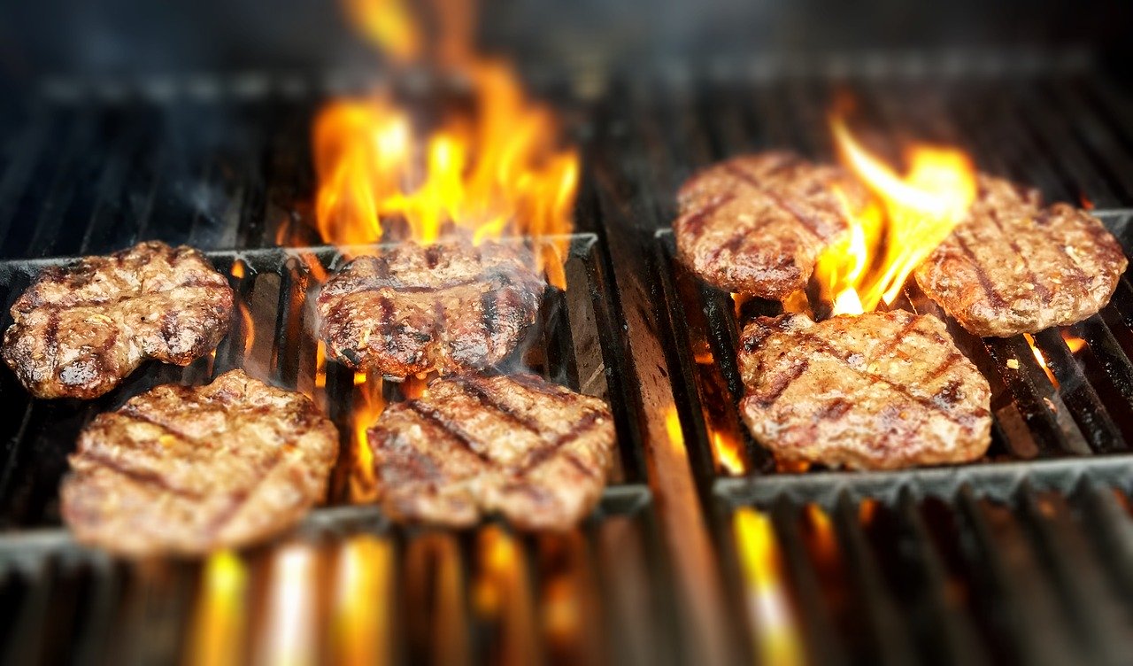 Close up of grill with 7 burger patties and flame.
