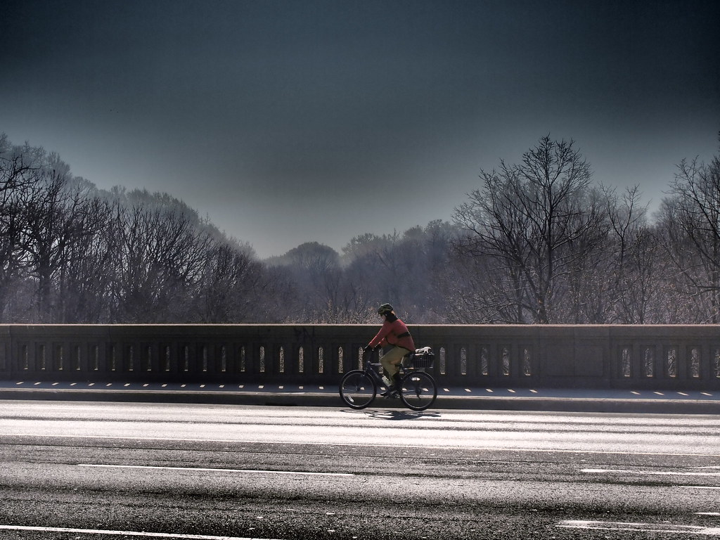 Female cyclist on bridge with snow-covered trees in background in Rosedale, Toronto.