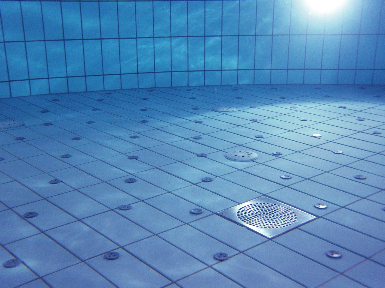 Photo of clear blue swimming pool water, tiles and drain.