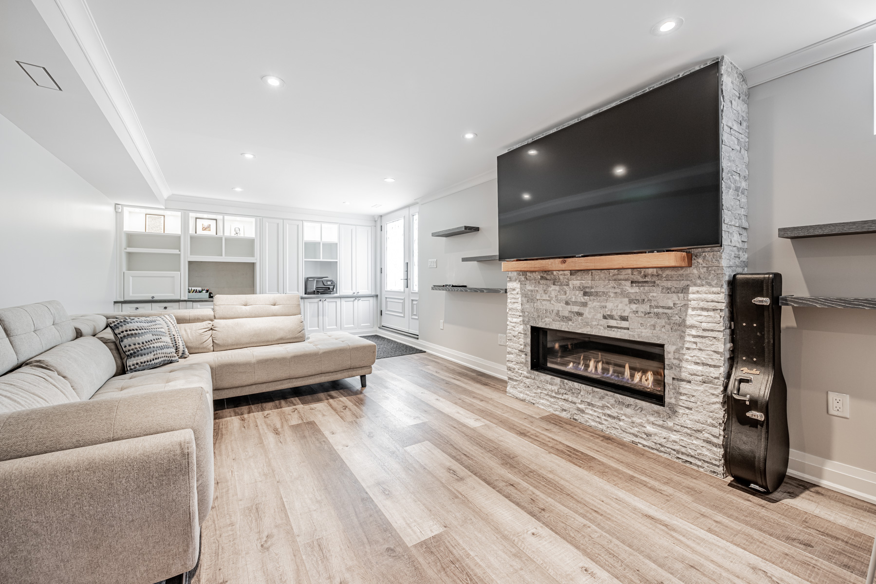 Finished basement with wide laminate planks and wall-mounted shelves.