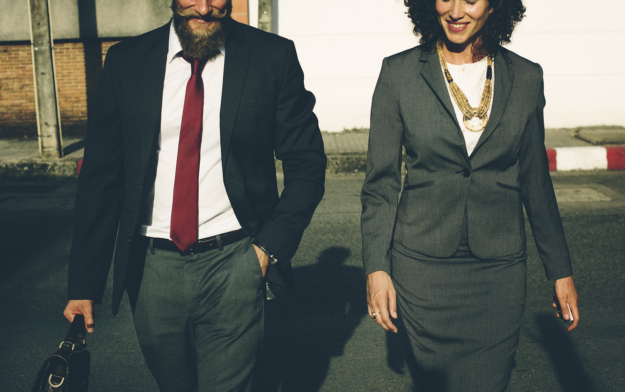 View of man and woman dressed in dark business attire walking.