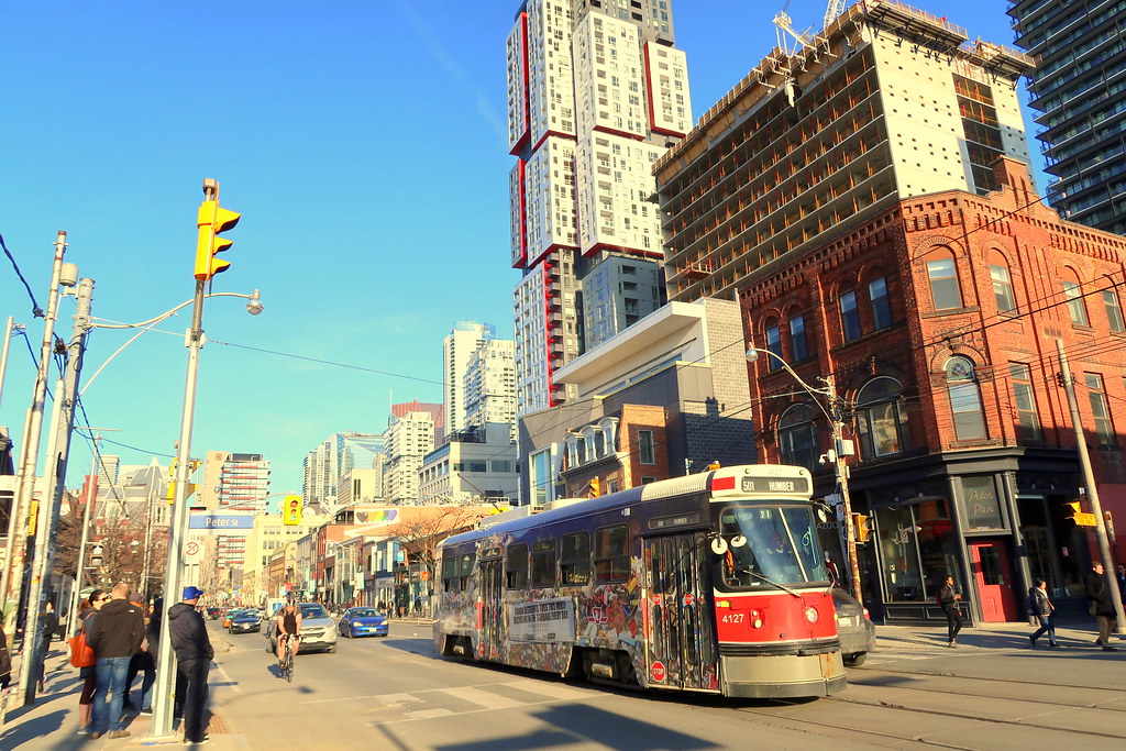 Pedestrians, cyclists, cars and red TTC streetcar on Queen St in Toronto's Entertainment District.