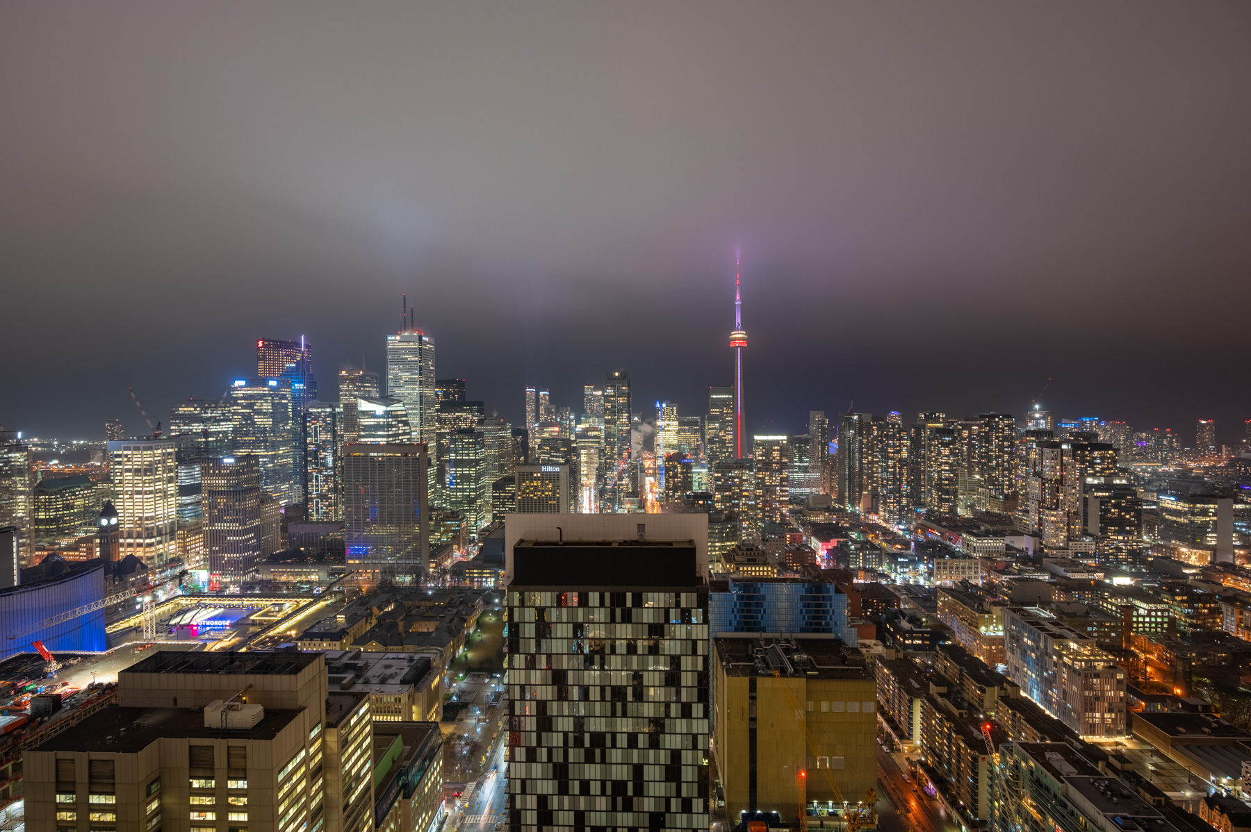 Toronto skyline at night with CN Tower glowing red and purple.