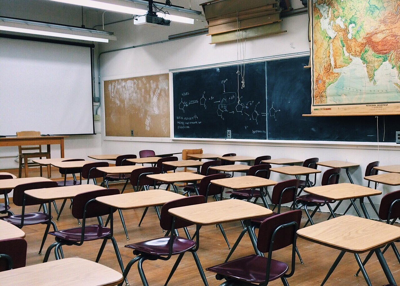 Empty classroom with chairs, desks, world map and blackboard with chemical formulas.