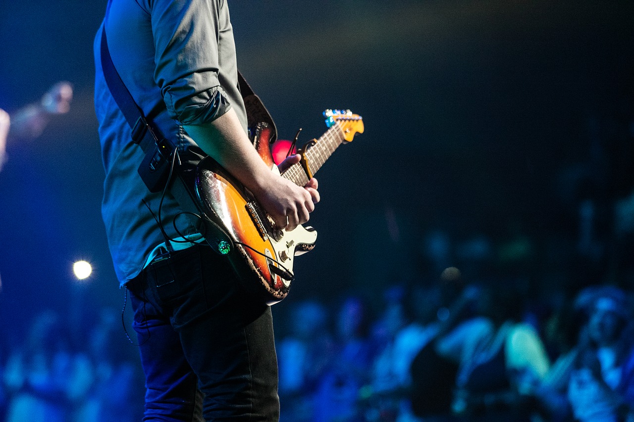 Behind the back view of man holding electric guitar on stage.