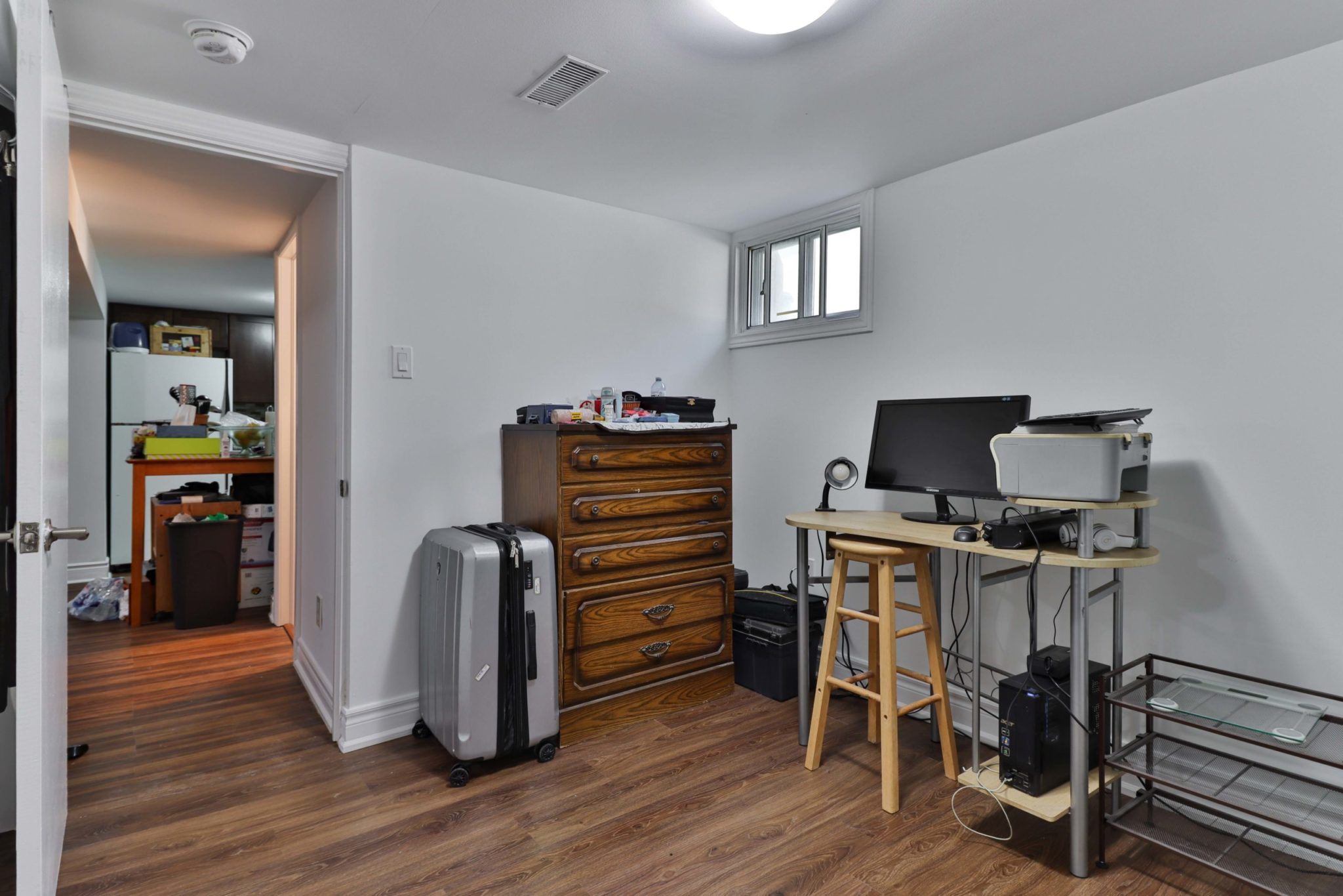 Basement office with computer, desk, large dresser, luggage and laminate floors.