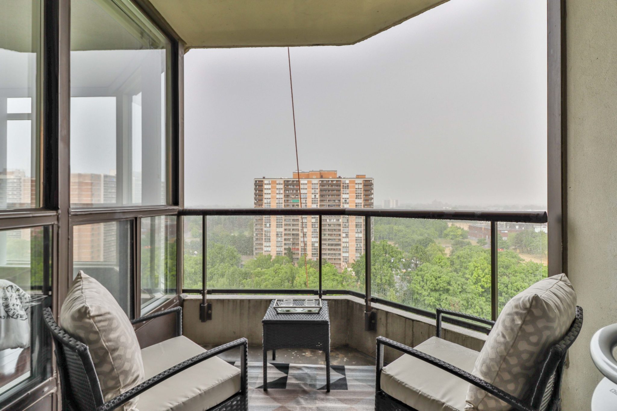 Condo balcony with concrete walls, glass panels, 2 chairs, table.
