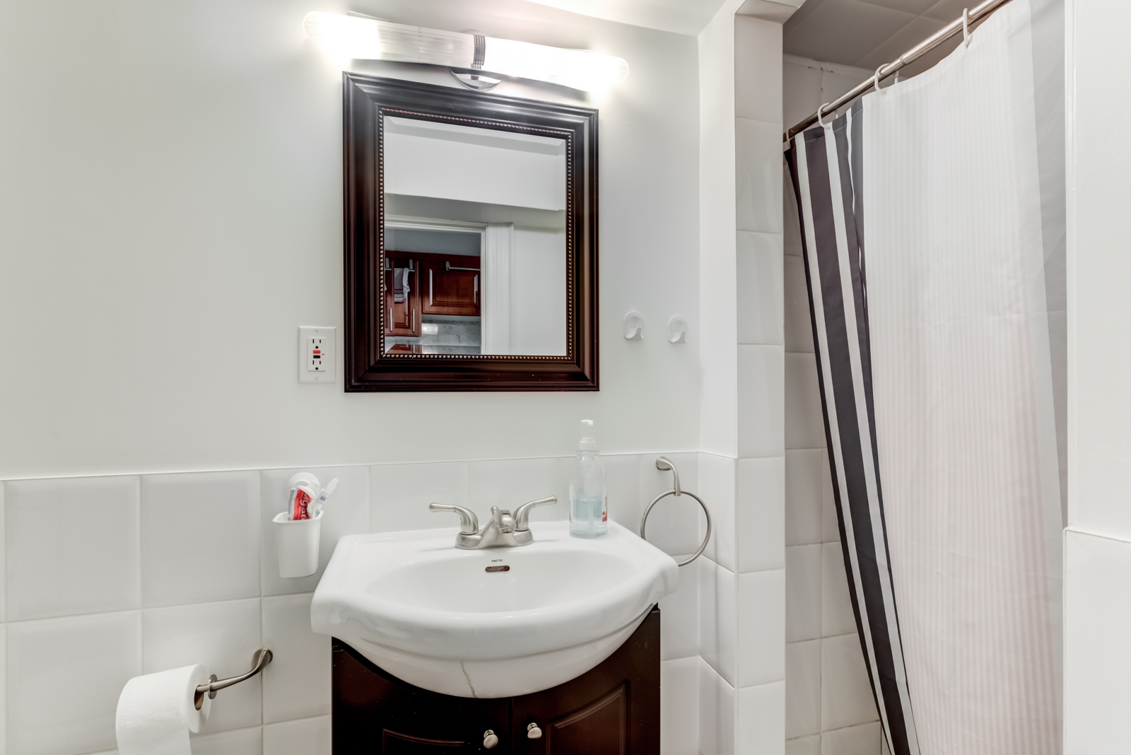 Super-simple washroom with gray white walls, tiles and shower curtain and brown cabinets.