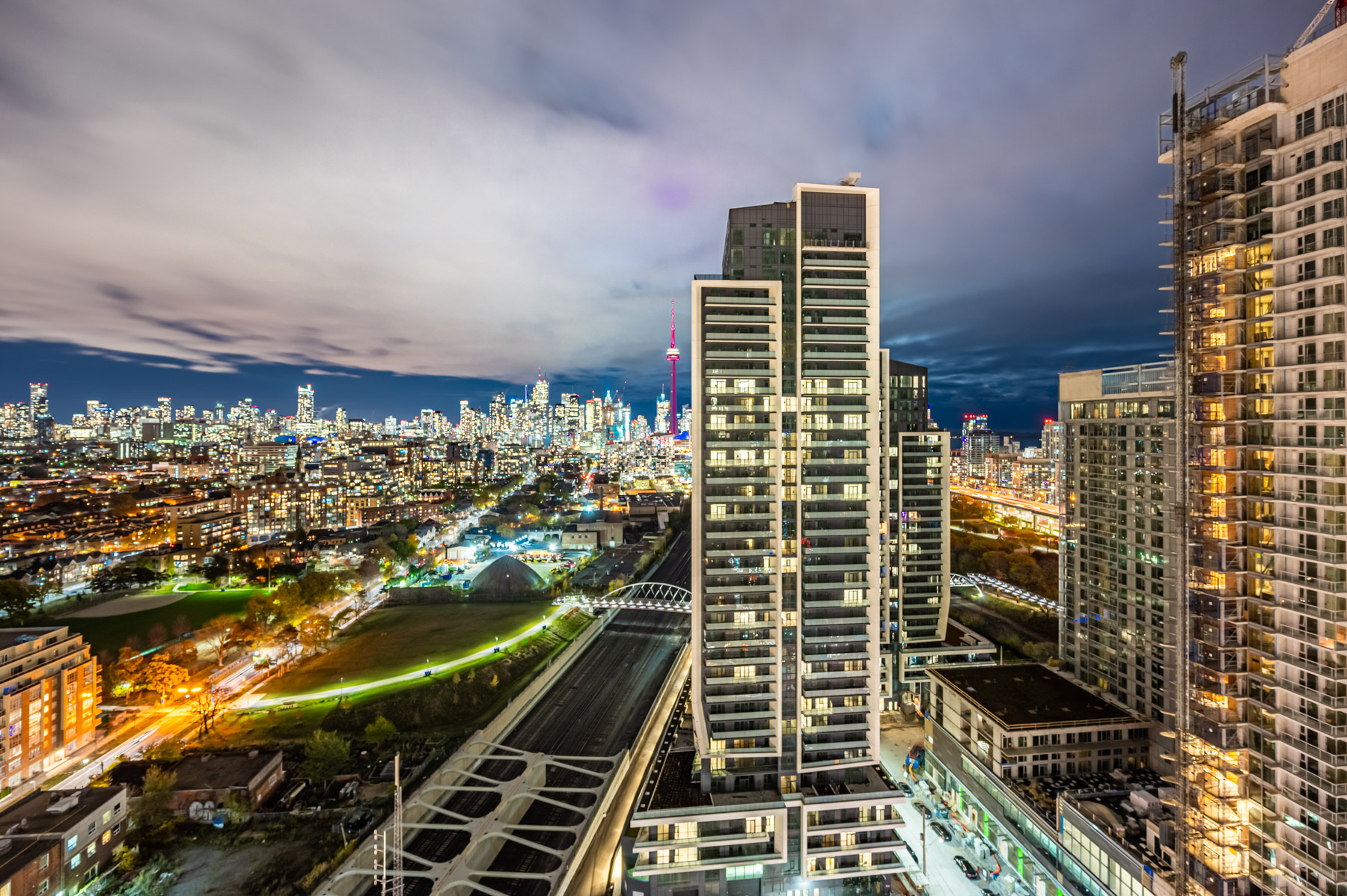 Toronto skyline at night with bright lights, buildings and red CN Tower in distance.