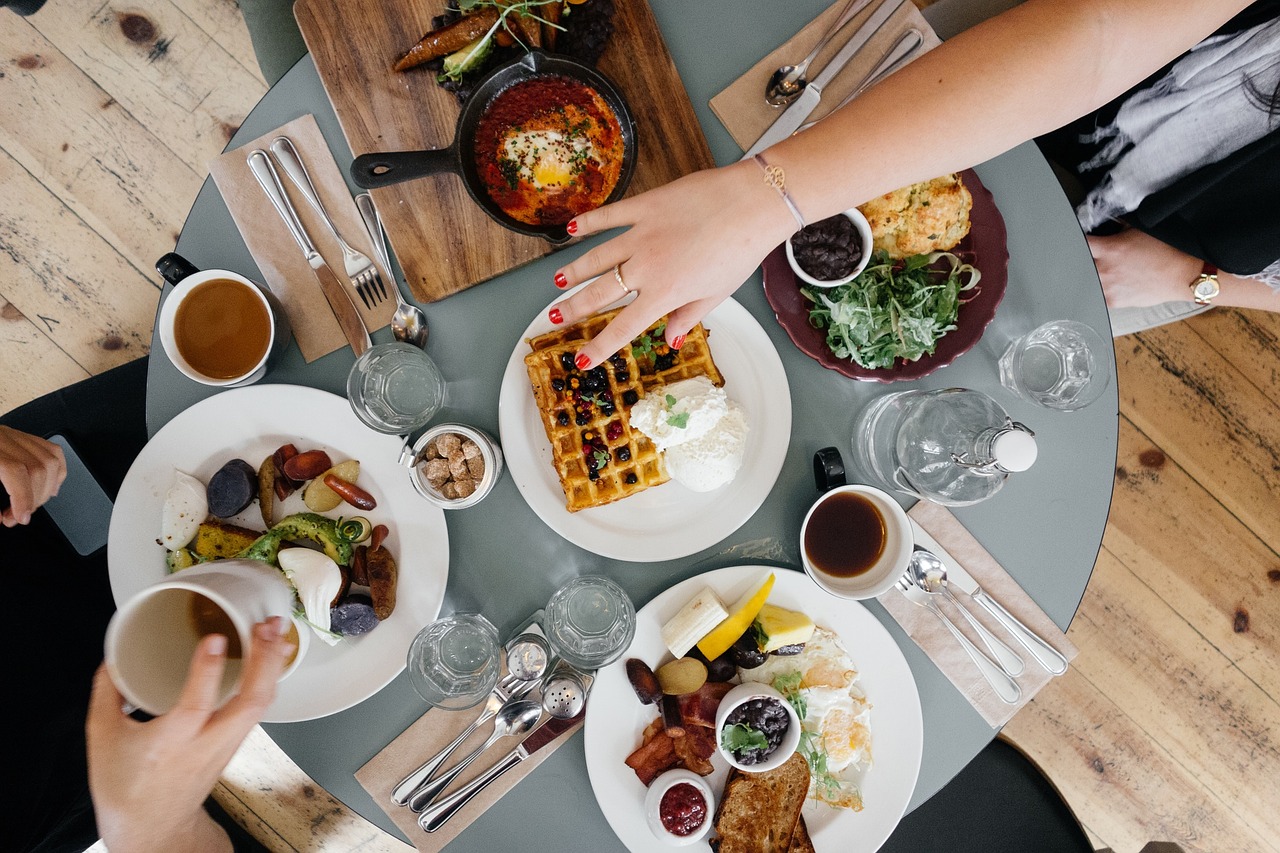 Top-down view of round breakfast table with food including fruits, vegetables and hand reaching for waffles.