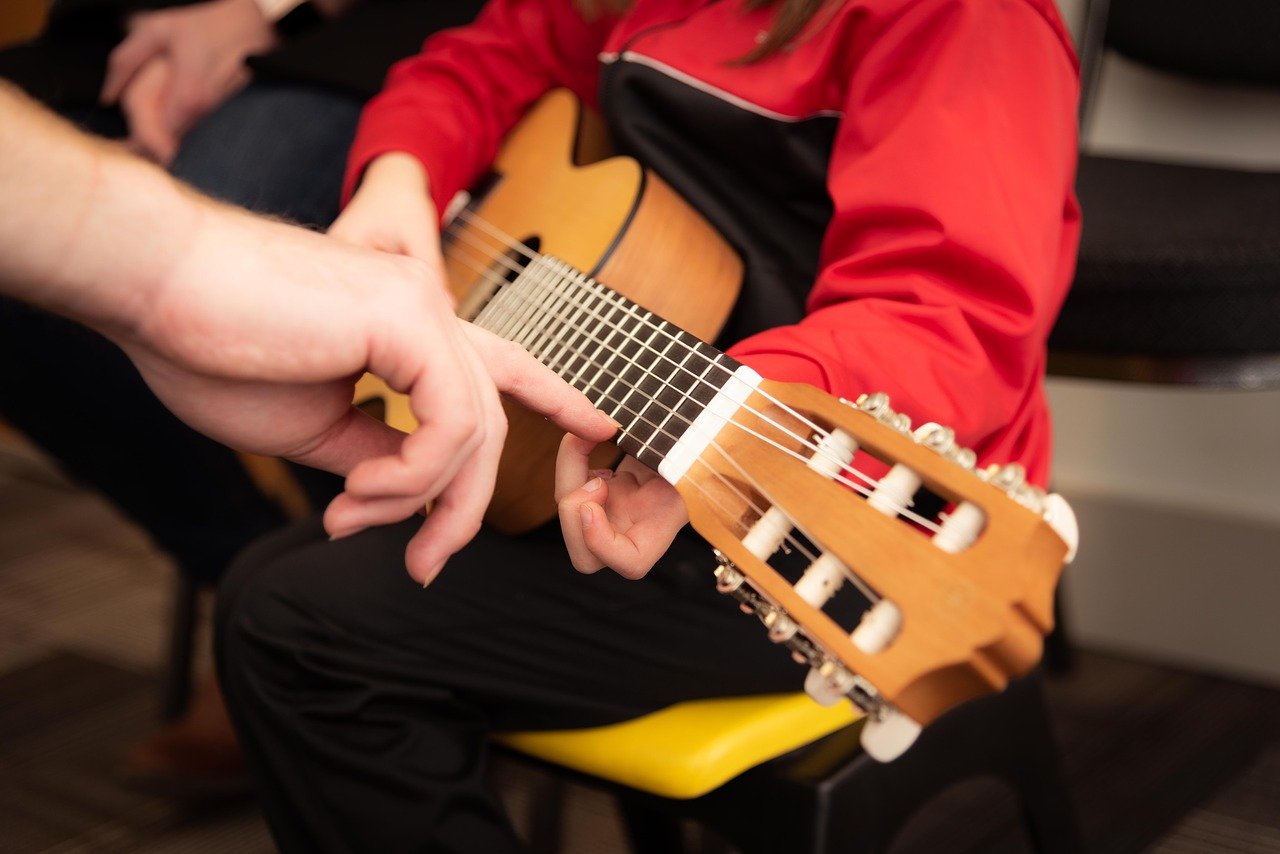 Close up of kid in red jacket learning to play guitar.