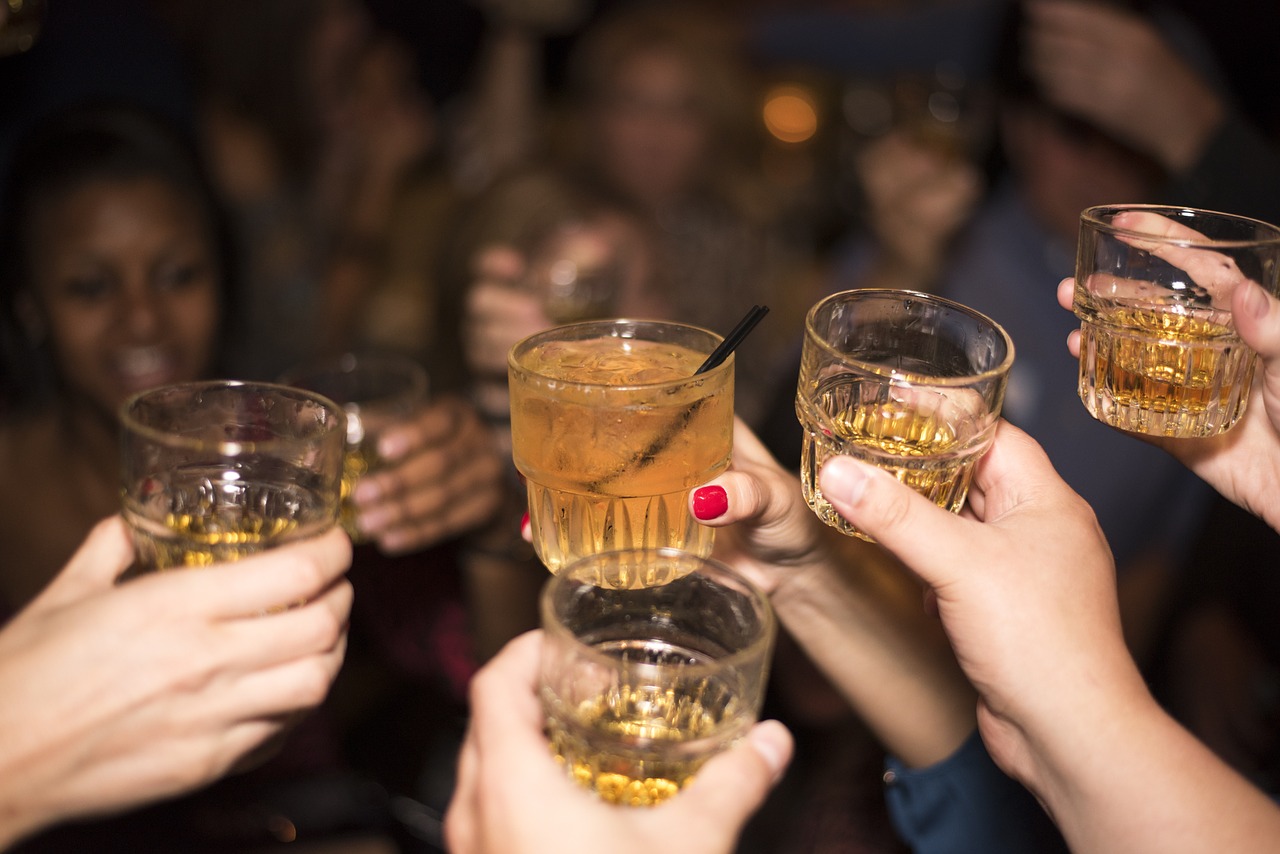 Close up of hands holding glasses of gold-coloured alcohol in celebration.