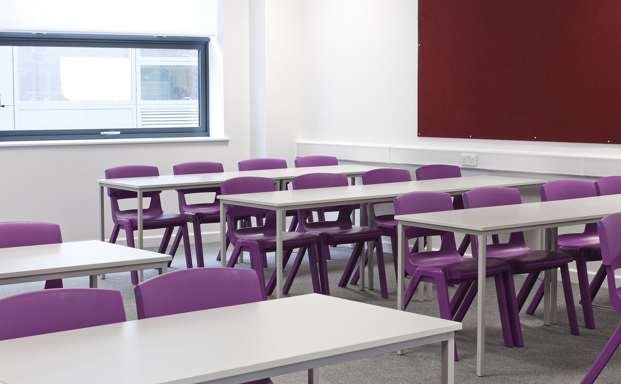 Empty classroom with white desk and purple chairs.