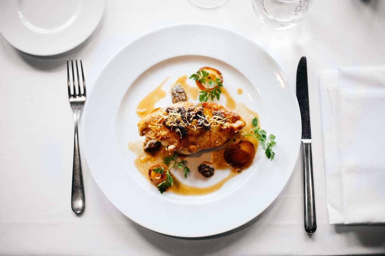 Top-down view of white dinner plate, fancy food and knife and fork.