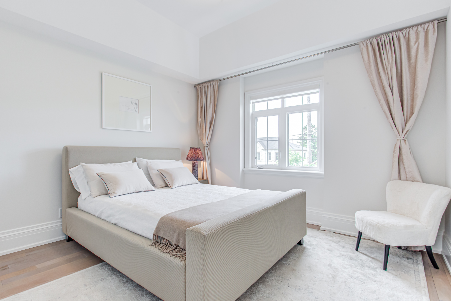 Large and elegant bedroom with gray walls, hardwood floors, bed and window.