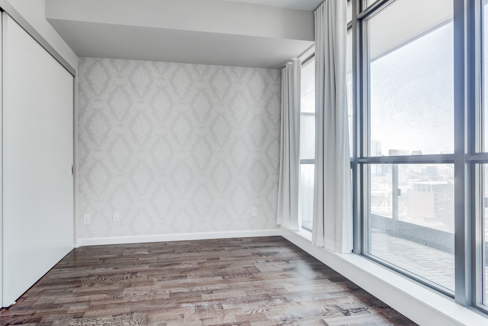 Empty master bedroom with huge windows, dark laminate floors and gray walls.