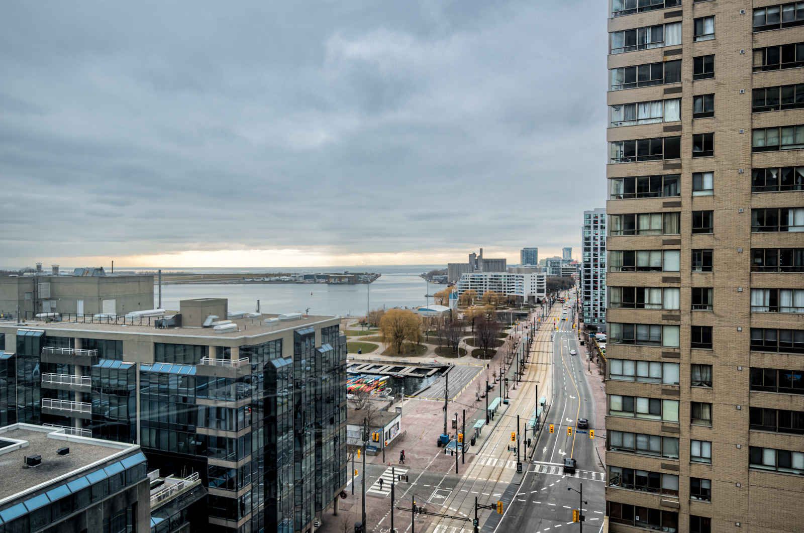 Balcony view of Lake Ontario, buildings, streets, cars and Billy Bishop Airport in distance.