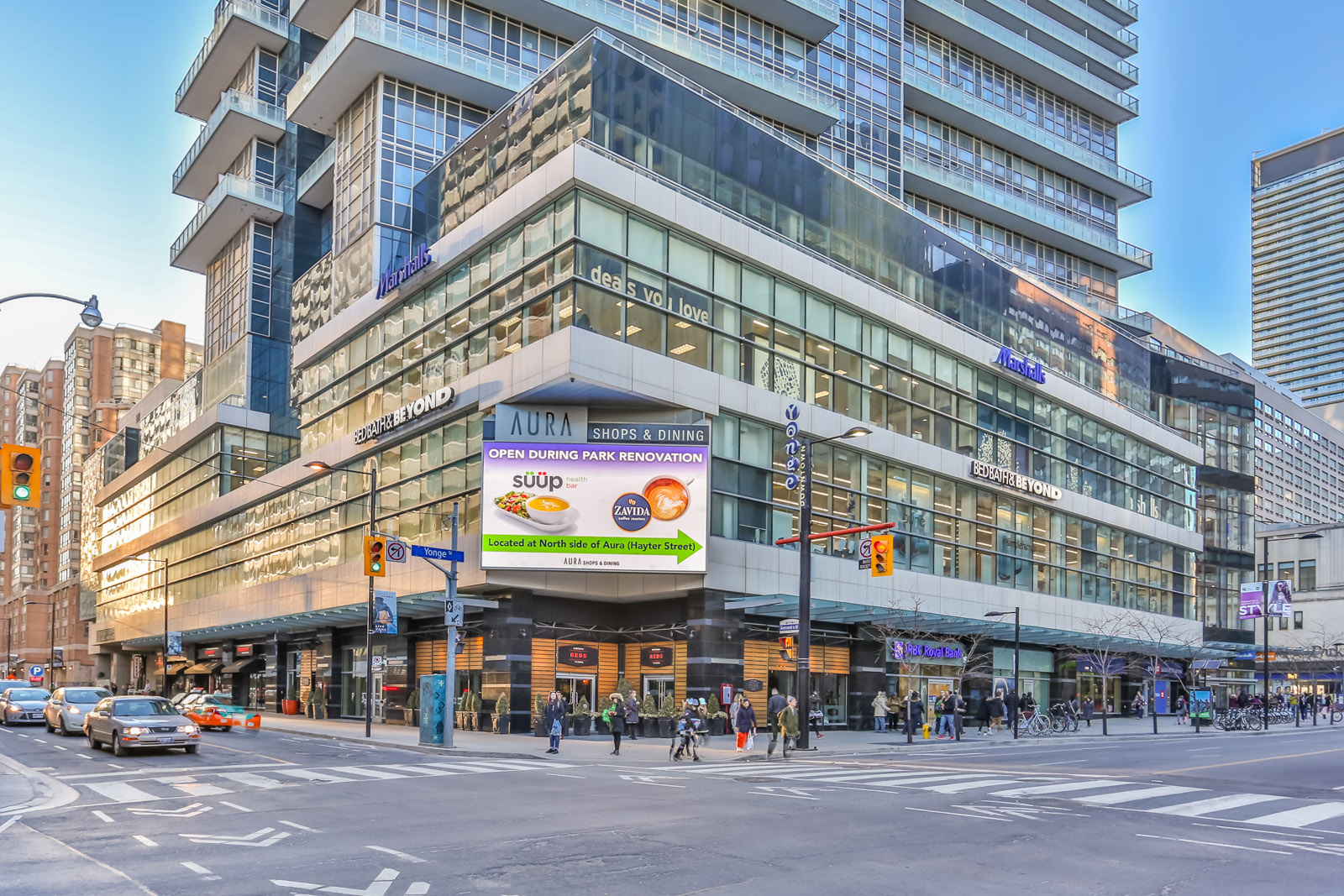 Image of Aura from across the street. The photo shows so many people, cars, and also signs. Furthermore, we can see the upper floors above the shops. seems like, maybe, probably, almost most of all, most noteworthy, especially relevant.