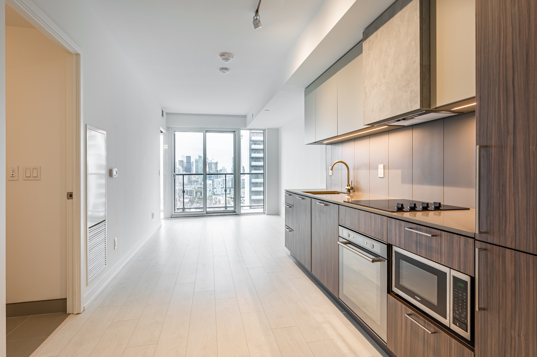 Empty condo kitchen, dining room, living room with warm colours and natural lighting.