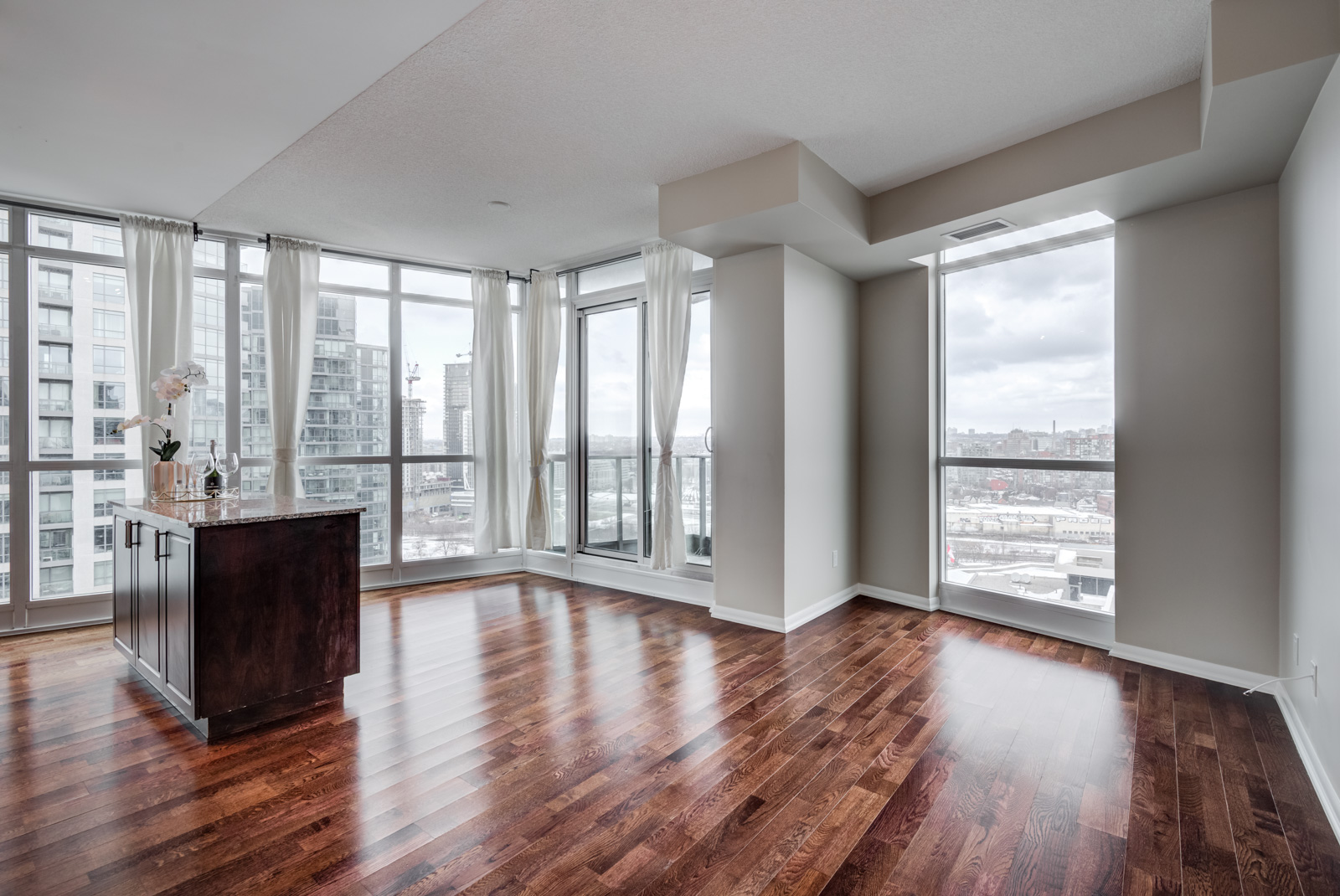 Empty condo unit of 215 Fort York Blvd with kitchen island, dark hardwood floors and several large windows.