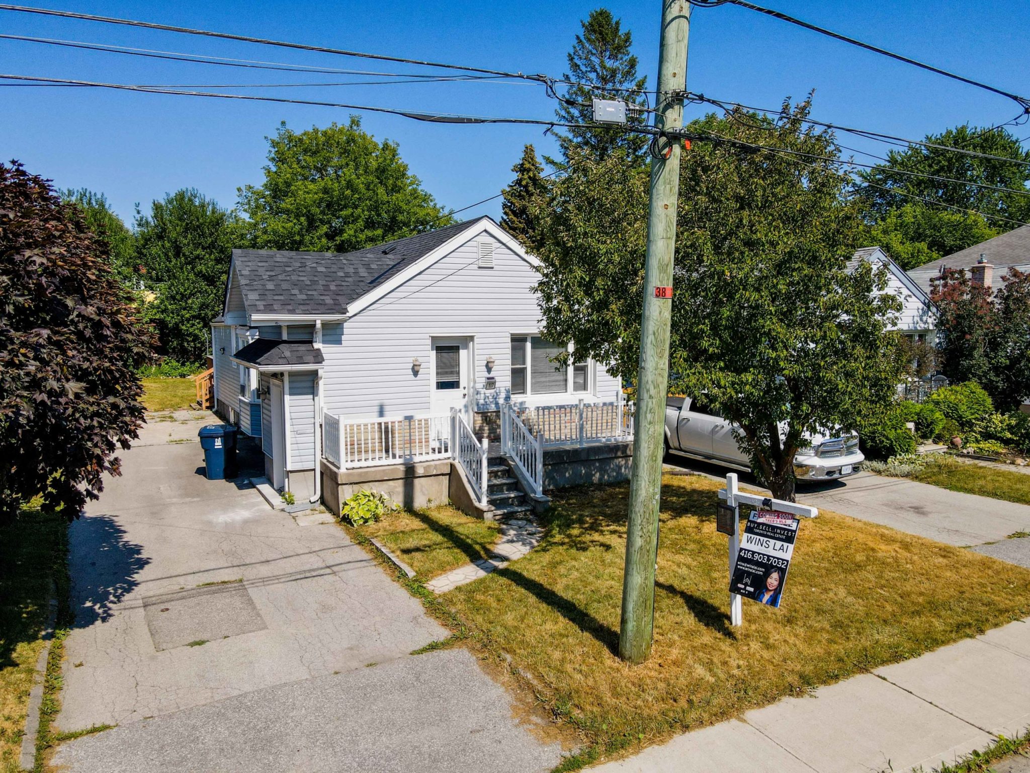 Front of 117 Phillip Ave, a bungalow with big driveway and front yard with tree and utility pole.