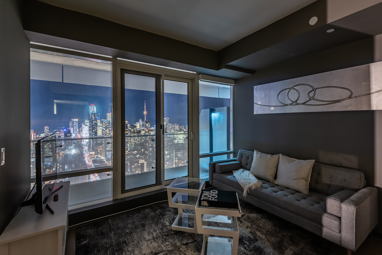 Living room at night with view of Toronto skyline through windows of 1 Bloor St
