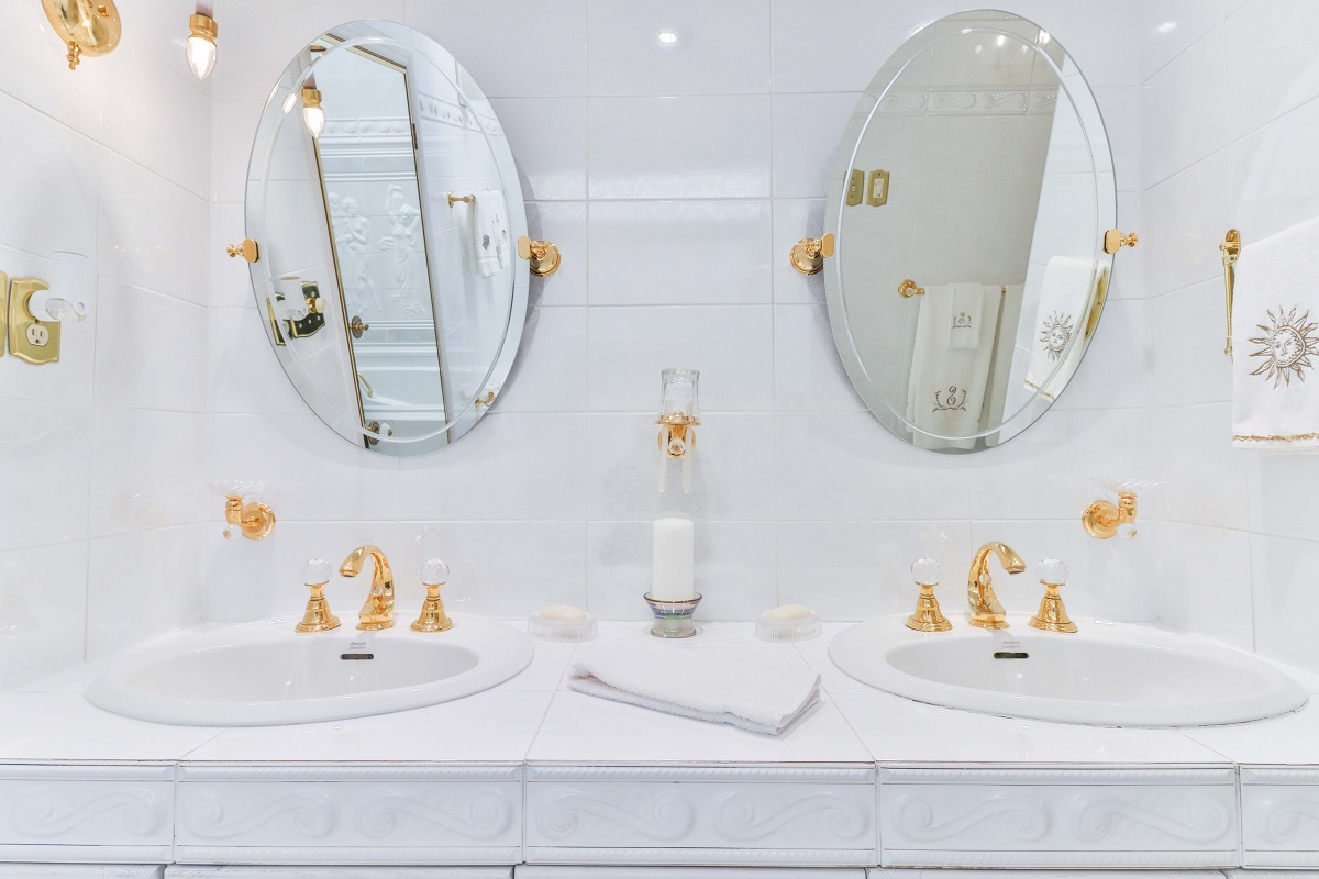 White bathroom with dual mirrors, sinks, and gold trims.