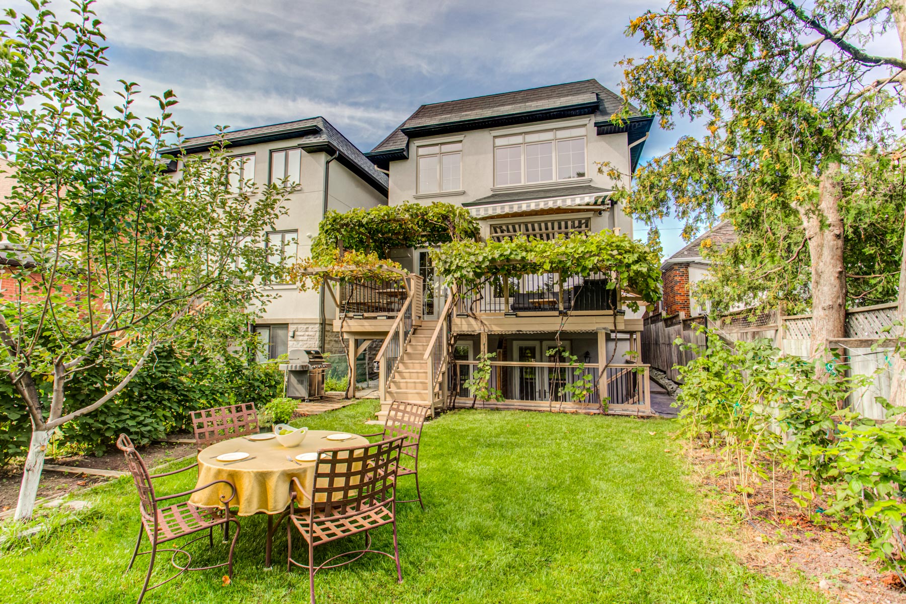 House backyard with trees, vines and garden plots.