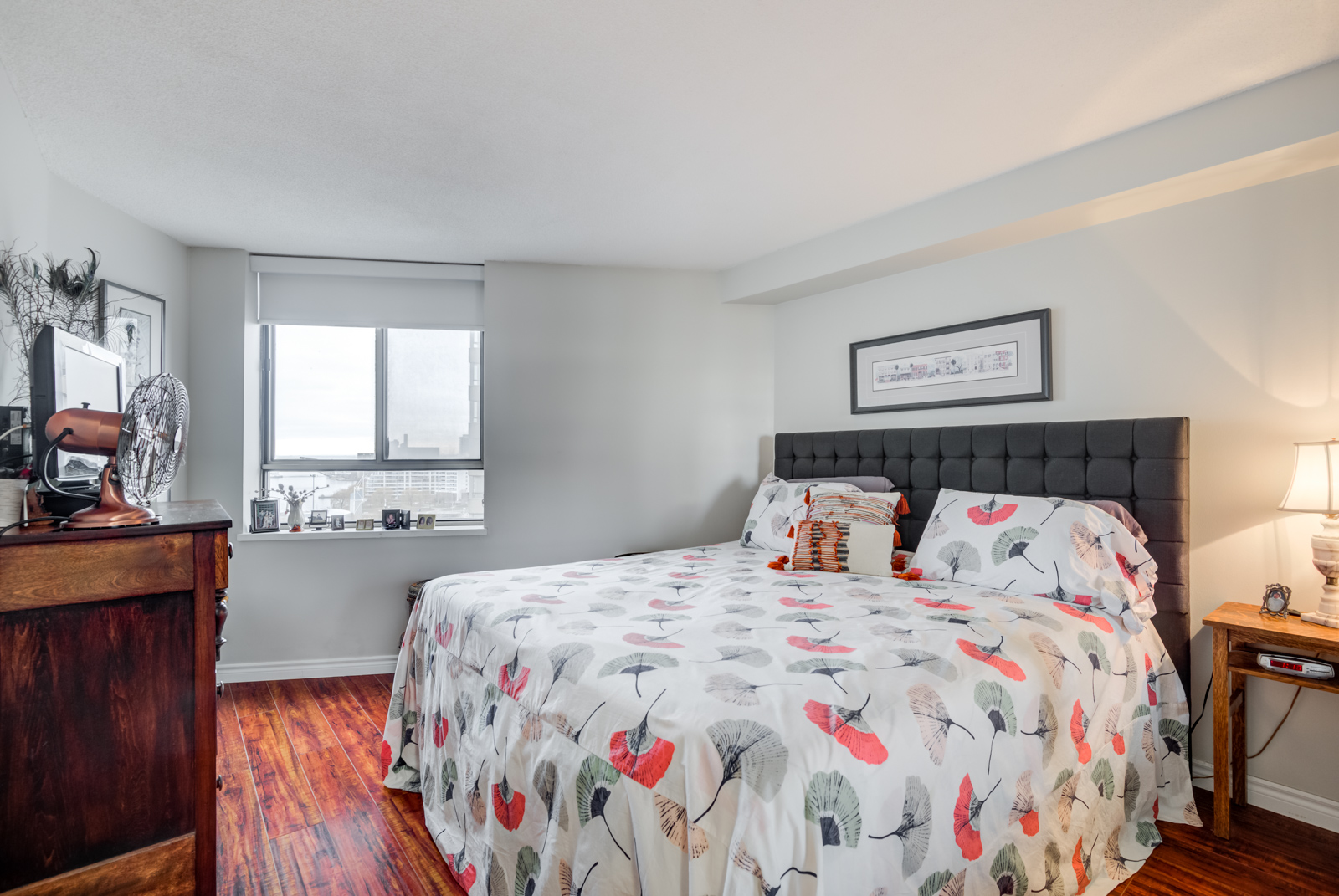 Large master bedroom with king-sized bed, red laminate floors and large window.