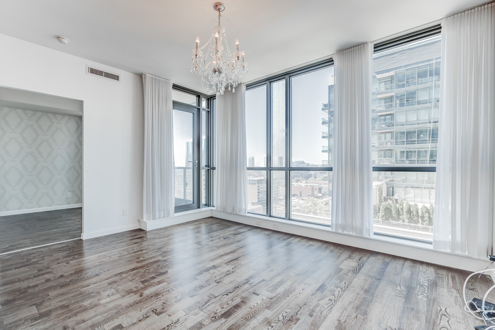 Condo interior with 9-foot ceilings, floor-to-ceiling windows, dark laminate floors, gray walls and chandelier.