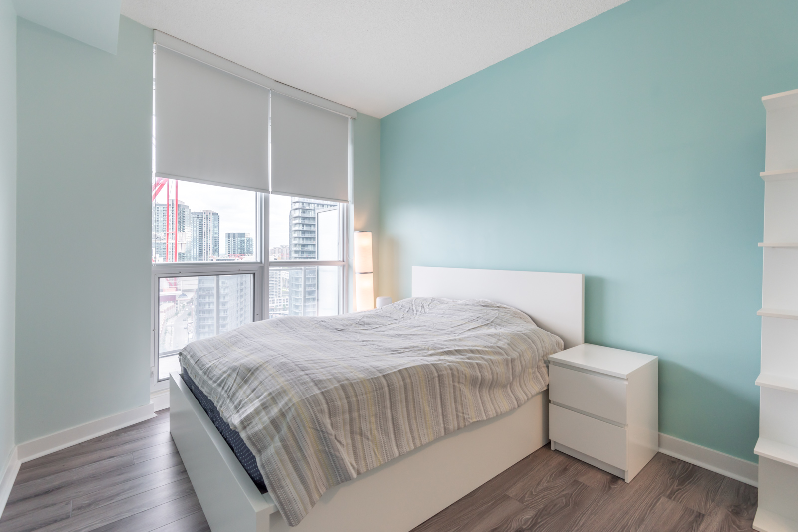 A photo of the master bedroom. We also see the windows and city behind them, and blue walls.