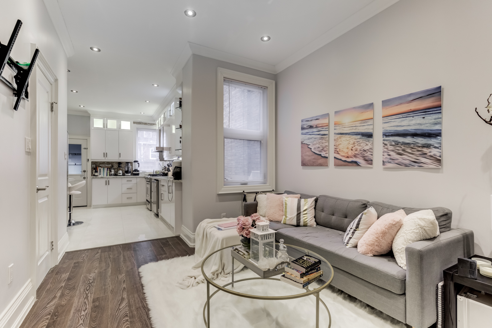 Renovated living room with gray sofa, thick white rug and gray walls hung with paintings.