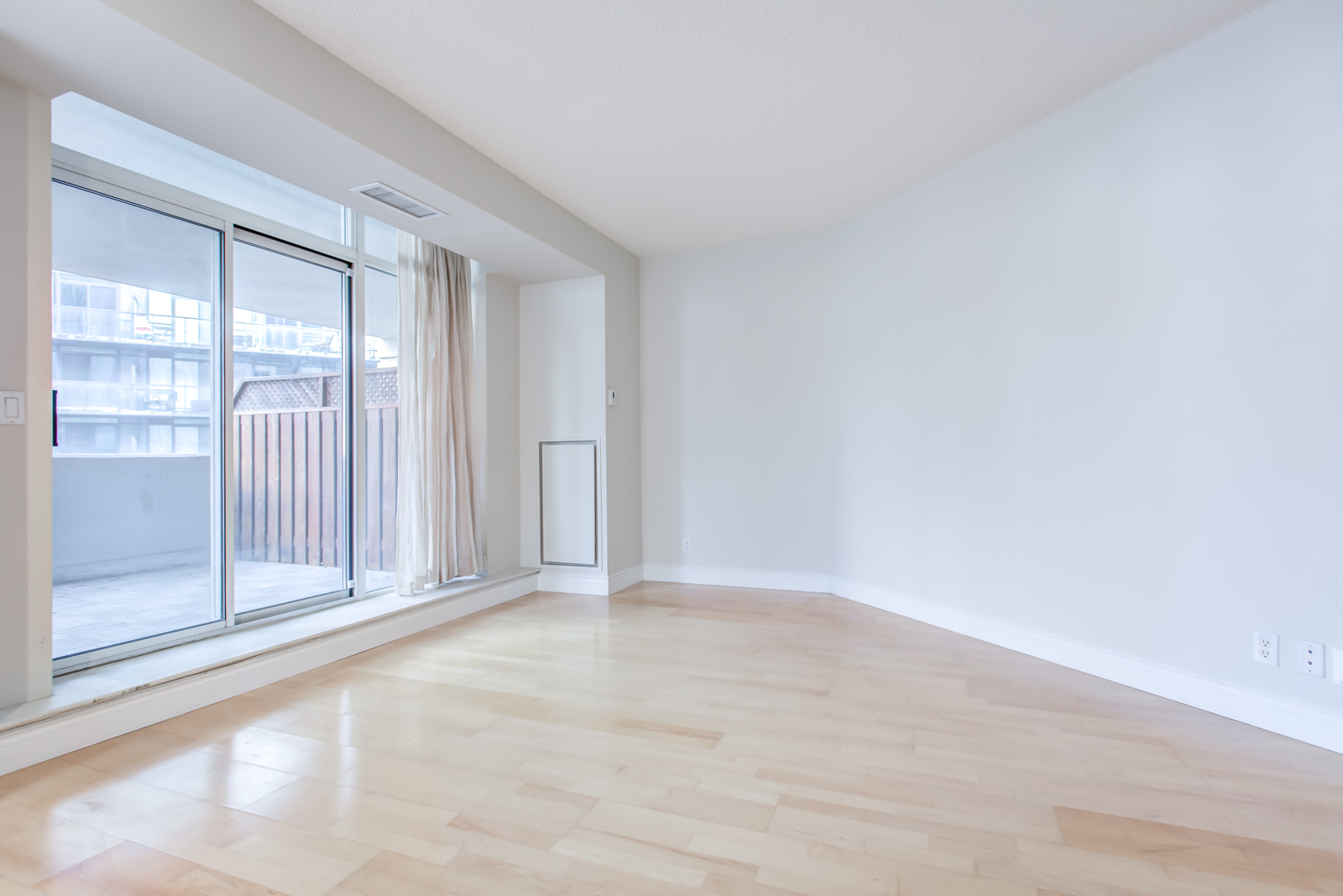 Empty living room with view of balcony through screen doors.