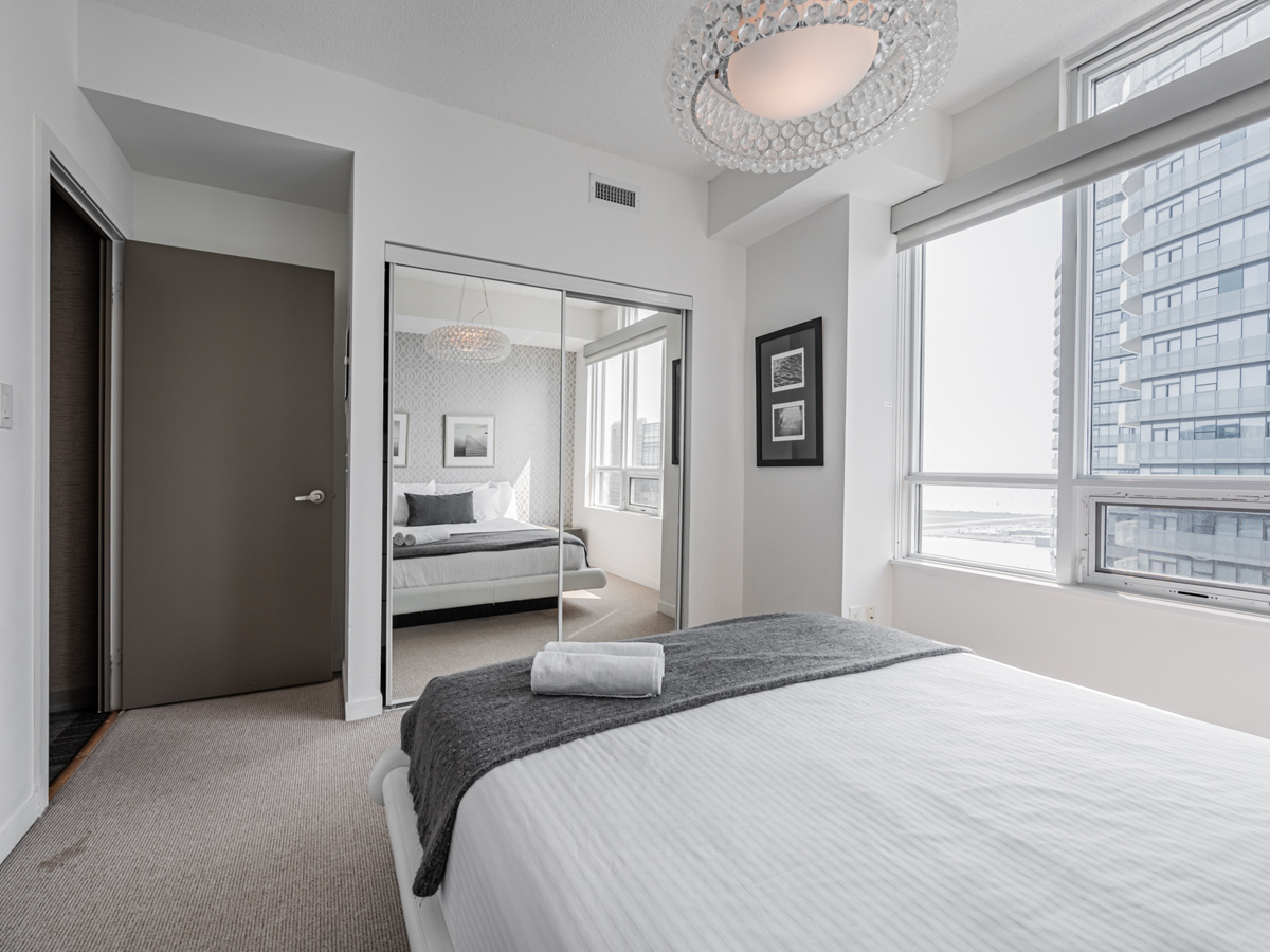 Condo bedroom with gray broadloom carpet and mirror door closet.