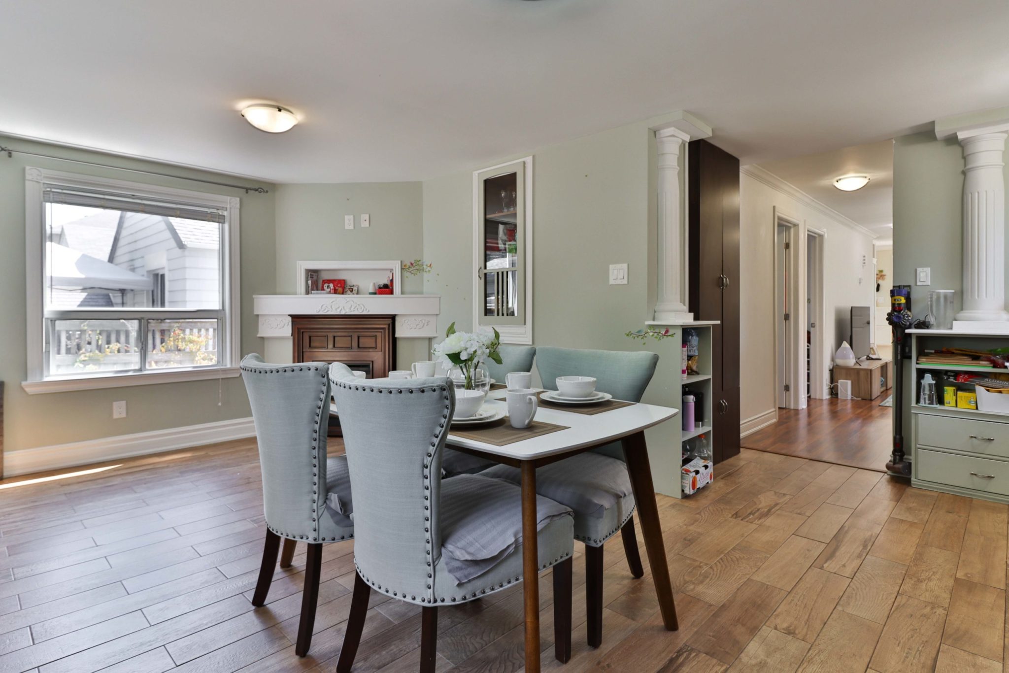 Large dining room with wood floors, white columns and green walls.