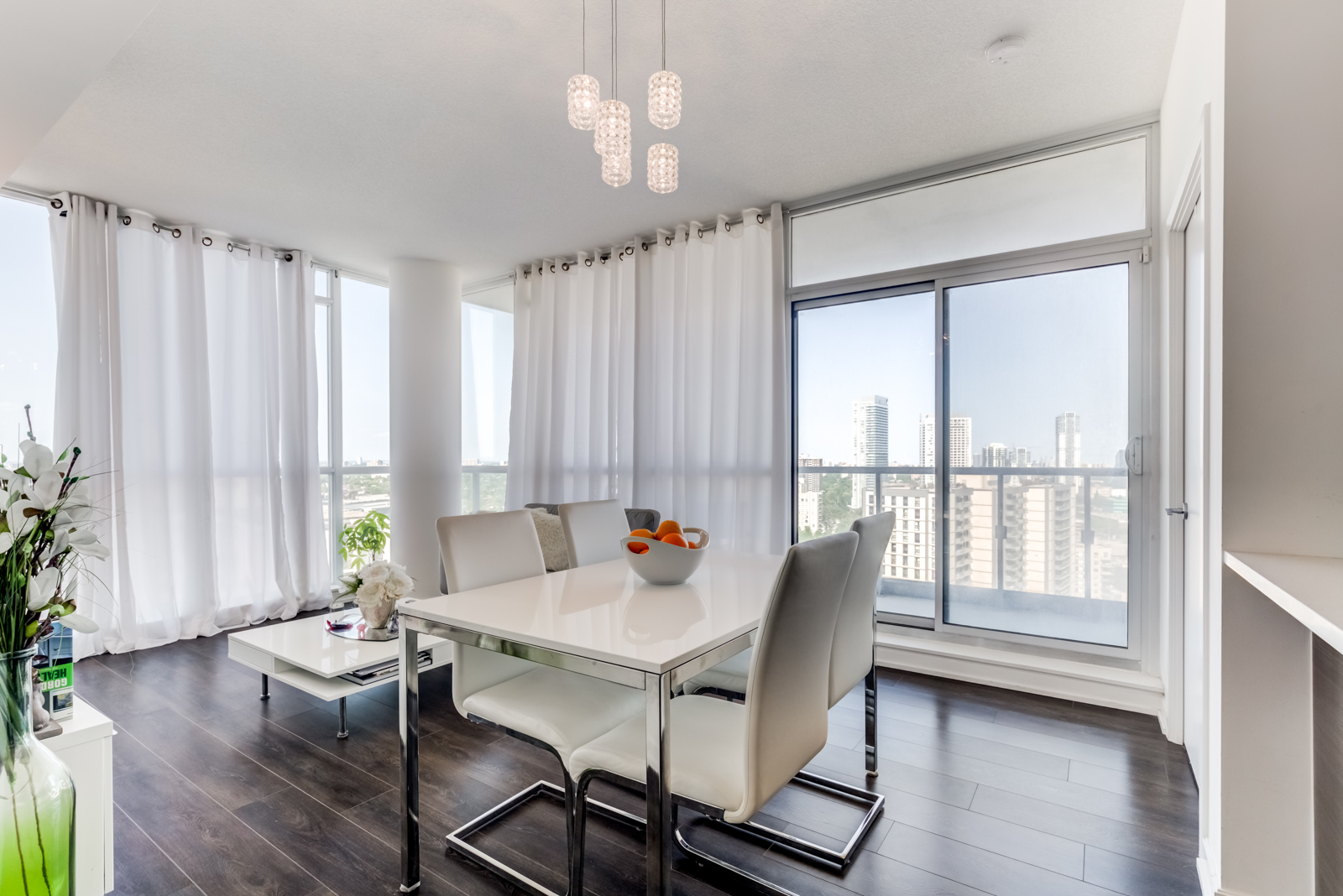 Elegant dining room with dark floors and white walls and curtains with open windows.